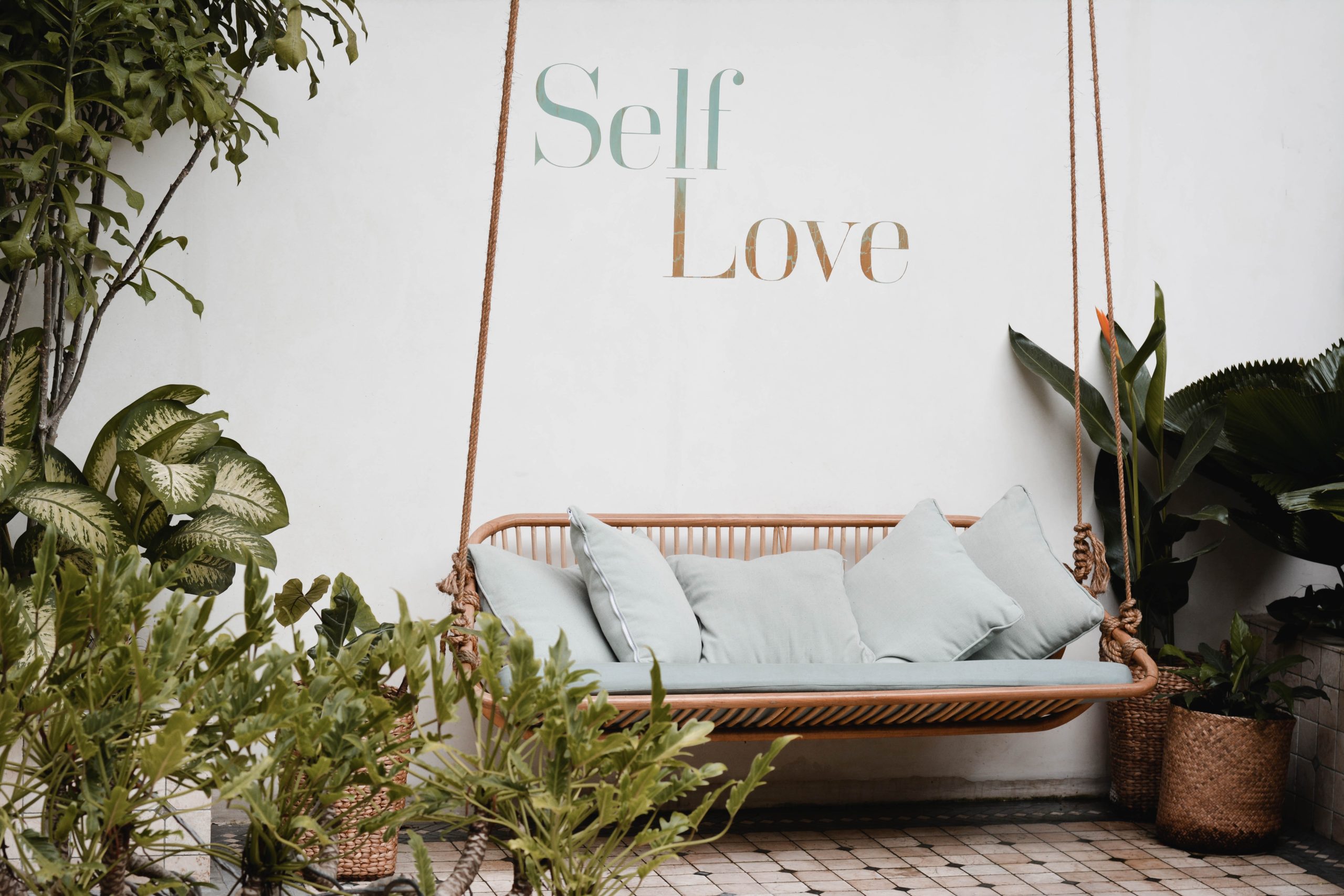 Self love sign over swinging couch surrounded by green plants